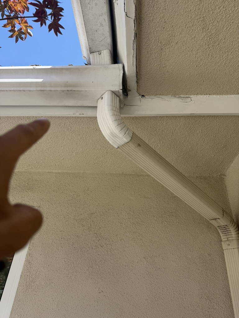 Cracked fascia board near downspout close-up